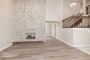 Two-story living area featuring a full-height brick fireplace, wood-finish flooring, a grand staircase with wood banister, and a decorative chandelier
