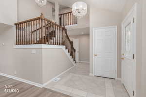 Two-story foyer featuring a wood staircase with balusters, a decorative chandelier, and light-toned tile flooring