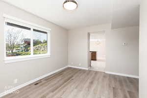 Spacious room featuring wood-finish flooring, a large window with white trim, and a contemporary ceiling light fixture