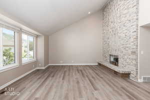 Spacious living area featuring a floor-to-ceiling brick-surround fireplace, vaulted ceiling, wood-finish flooring, and multiple windows