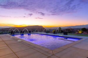 In-ground swimming pool with integrated spa and water features, surrounded by a stone paver patio