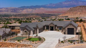 Expansive property featuring a contemporary stucco and stone exterior, multi-car garage, concrete driveway, private tennis court, and desert landscaping with mountain scenery