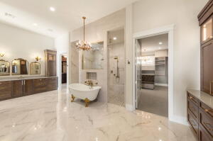 Spacious bathroom featuring a freestanding clawfoot tub, dual shower heads within a glass-enclosed shower, extensive vanity with three framed mirrors, and a chandelier light fixture
