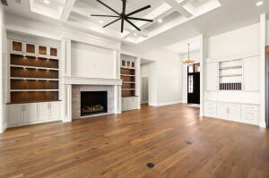 Expansive living space featuring wood-finish flooring, a coffered ceiling with a modern ceiling fan, and a fireplace with a stone surround
