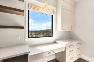 Integrated desk area featuring a large window, built-in cabinetry, wood-finish floating shelves, and a decorative chandelier