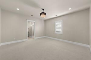 Spacious room featuring neutral wall tones, recessed lighting, a decorative chandelier, white baseboards, and a window with plantation shutters