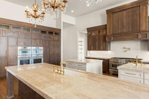 Spacious kitchen featuring an expansive island with a light-toned countertop, floor-to-ceiling wood cabinetry, dual built-in ovens, and a custom wood range hood
