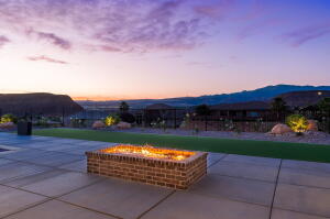 Expansive outdoor patio featuring a built-in brick fire pit, large format concrete pavers, artificial turf, and a mountain backdrop