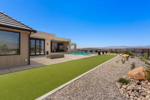 Rear exterior featuring a large patio, built-in pool, artificial turf, and xeriscaped rock garden with mature desert plantings