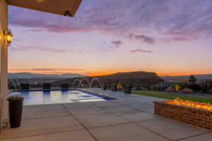 Expansive patio featuring a rectangular swimming pool with water features, a built-in brick fire pit, and a mountain backdrop