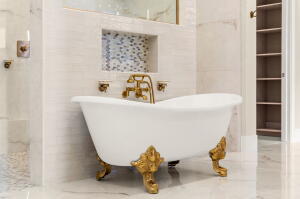Freestanding white clawfoot tub with ornate gold-tone feet and matching brass fixtures
