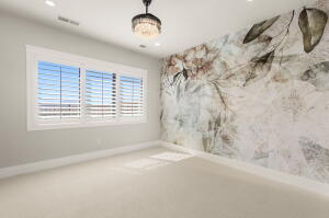 Spacious room featuring a decorative accent wall, three large windows with white plantation shutters, neutral carpeting, recessed lighting, and a crystal chandelier