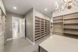 Expansive walk-in closet featuring extensive built-in shelving, a central island with a light-toned countertop, recessed lighting, and an ornate chandelier