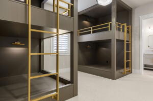 Built-in bunk beds featuring a matte dark gray finish, gold-tone metal ladders, integrated lighting, and a white shuttered window