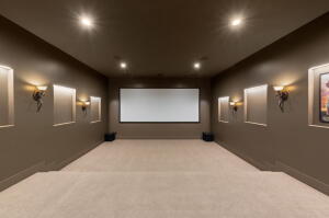 Dedicated media room featuring a large projector screen, recessed ceiling lighting, and wall-mounted sconces