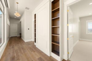Hallway featuring wood-finish flooring, built-in shelving, white paneled walls, and a decorative pendant light fixture