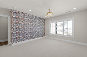 Spacious room featuring patterned accent wall, white plantation shutters, recessed lighting, and a crystal chandelier