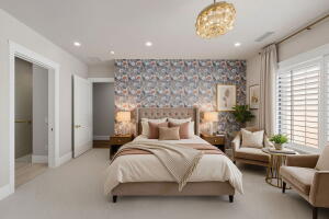 Carpeted room featuring a patterned accent wall, a tufted headboard, and a contemporary chandelier