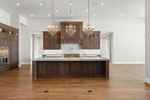 Spacious kitchen featuring an expansive center island, warm wood cabinetry, stainless steel double ovens, wood-finish flooring, and recessed lighting