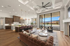 Spacious open-concept interior featuring light wood-finish flooring, a coffered ceiling with recessed lighting and a large ceiling fan, and extensive floor-to-ceiling windows
