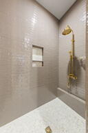 Shower enclosure featuring light-toned subway tile walls, a built-in shower niche, and a gold-finish shower fixture