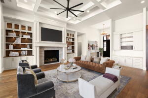 Spacious living area featuring coffered ceilings, wood-finish flooring, a fireplace with a mantel, and built-in shelving with cabinetry