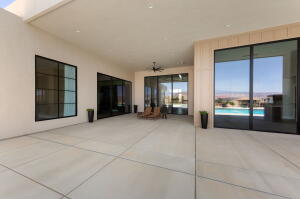 Expansive concrete patio area with a covered ceiling, featuring multiple large glass sliding doors and a prominent window with dark framing