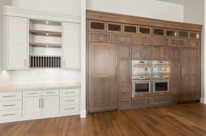 Expansive kitchen wall featuring integrated ovens, custom cabinetry, wood-finish flooring, recessed lighting, and a white subway tile backsplash