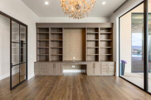 Wood-finish flooring throughout this room featuring a crystal chandelier, built-in shelving with integrated cabinetry, and large black-framed glass doors