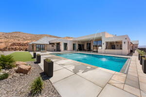 Expansive outdoor living area featuring a rectangular swimming pool with water features, a spacious concrete paver patio, and low-maintenance landscaping
