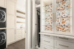 Laundry room featuring stacked front-load machines, white cabinetry, wood-finish shelving, and a built-in sink with a gooseneck faucet