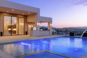 Outdoor pool area featuring a rectangular pool with water features, a spacious patio, and a modern exterior facade with large glass sliding doors