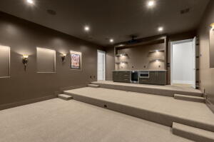 Tiered media room featuring recessed lighting, wall sconces, built-in cabinetry with integrated appliances, and wall-mounted shelving with accent lighting