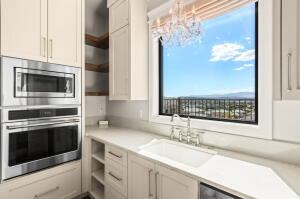 Kitchen featuring stainless steel built-in microwave and oven, recessed shelving, neutral cabinetry, a single basin sink with a chrome faucet, and a large window with city and mountain scenery