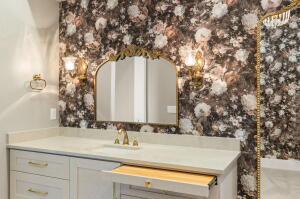 Vanity space featuring floral wallpaper, an arched mirror with a gold-tone frame, and two wall-mounted sconces