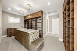 Custom closet featuring extensive built-in shelving, a central island with drawer storage, and integrated bench seating