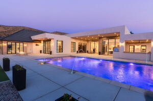 Exterior showcasing a rectangular swimming pool with integrated lighting, a spacious concrete patio, and a modern architectural design with large windows and glass doors