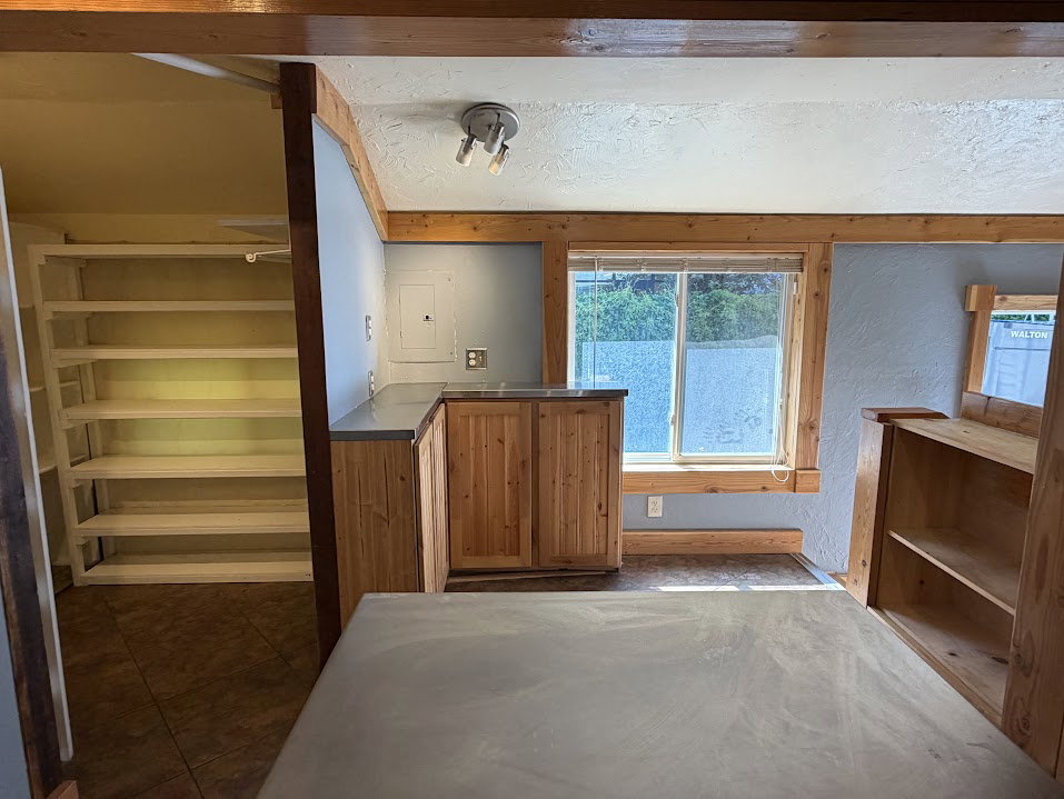 Wood-finish cabinetry with a light-colored countertop, recessed window with wood trim, built-in shelving, and exposed wood beams