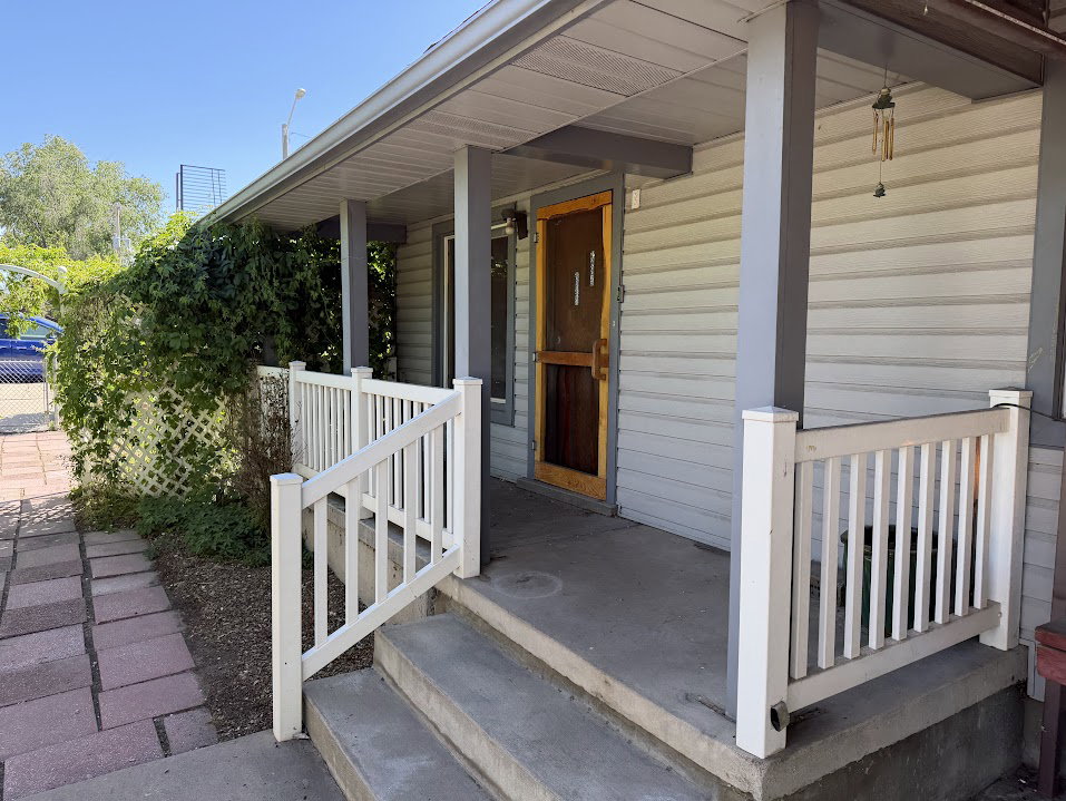 Front porch entry featuring a wood-finish screen door, light gray siding, and white railing
