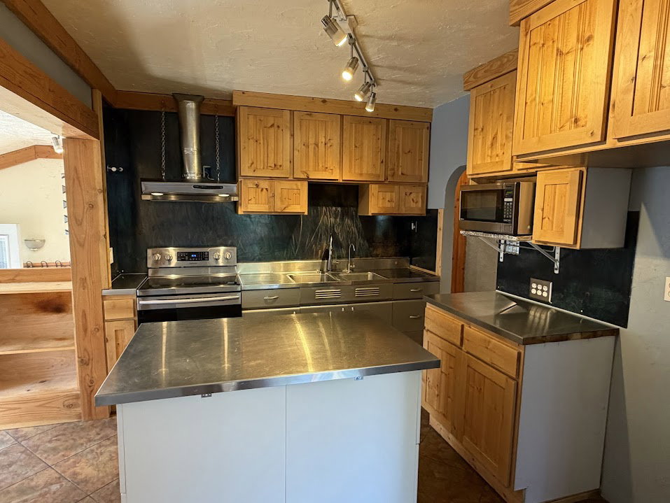 Kitchen featuring stainless steel appliances, wood cabinetry, a center island with a stainless steel countertop, and track lighting