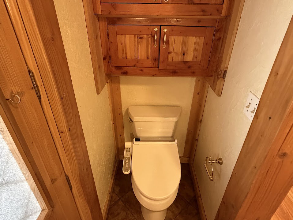 Powder room featuring a bidet toilet, wood-finish wall paneling, tile flooring, and integrated wood cabinetry with metal hardware