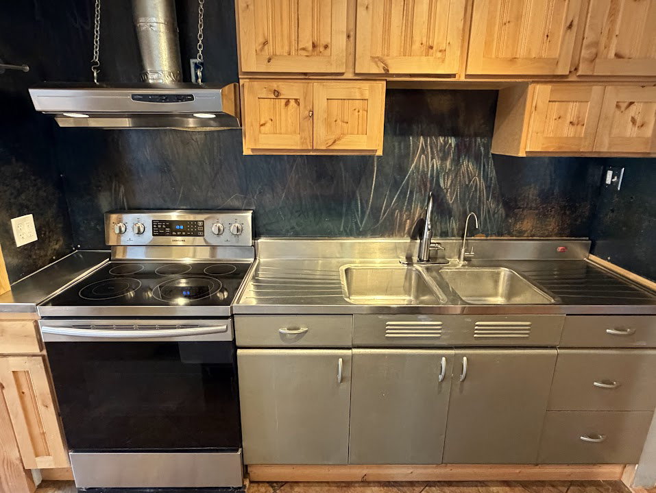 Kitchen featuring a stainless steel electric range, an overhead range hood, and a dual basin sink