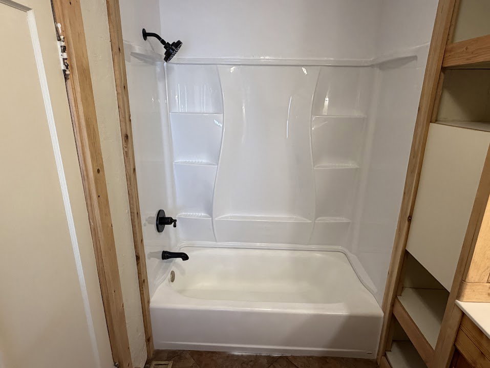 White acrylic tub and shower combination with integrated shelving, complemented by matte black fixtures