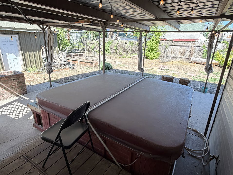 Covered patio area featuring a built-in spa with a cover, string lighting, and a corrugated metal roof