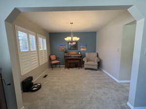 Carpeted interior space featuring a central chandelier, multiple windows with white plantation shutters, and a distinct accent wall