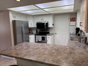 Kitchen featuring white cabinetry, stainless steel appliances, speckled countertops, and an integrated ceiling light panel
