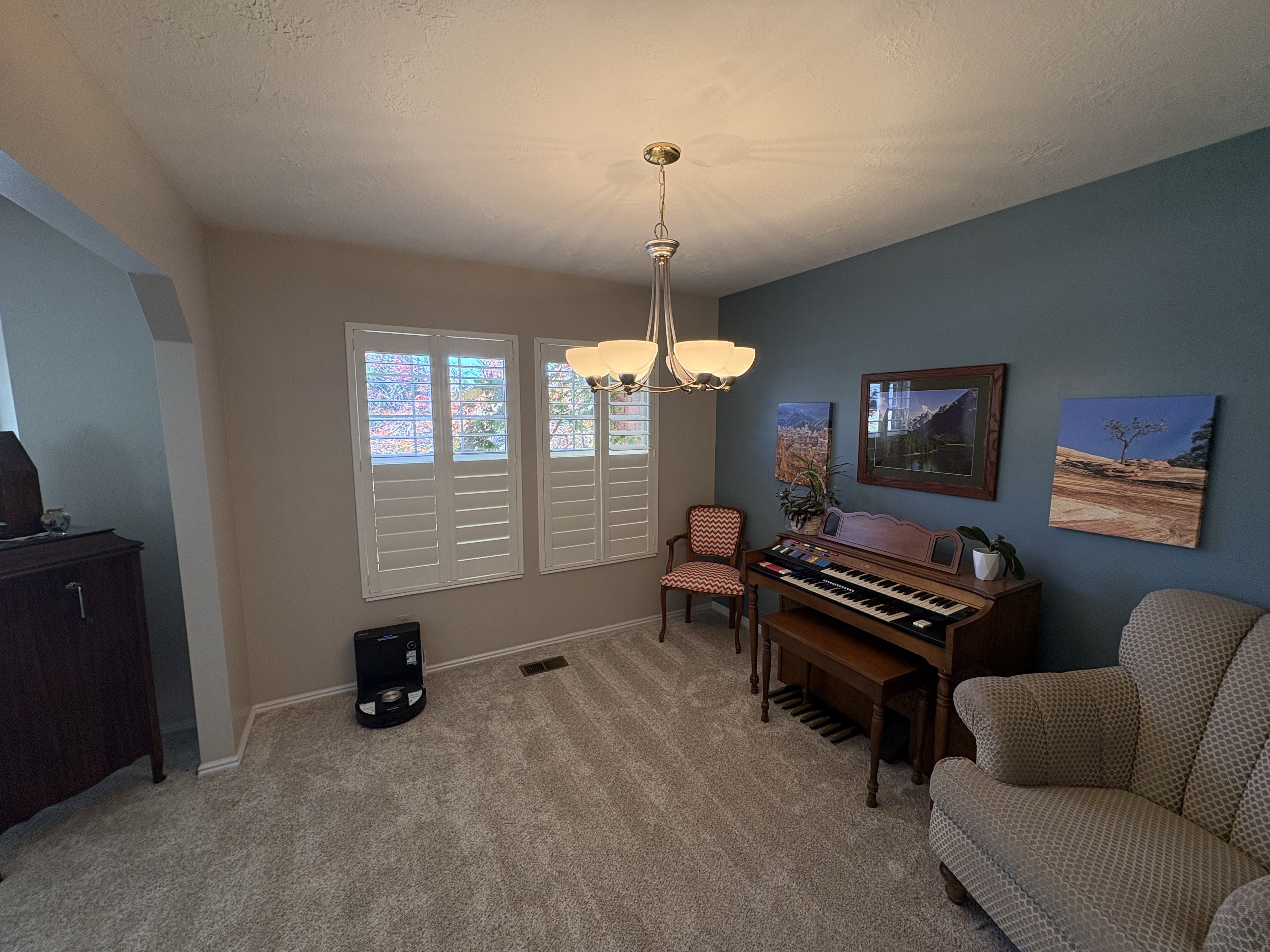 Carpeted room featuring a ceiling-mounted light fixture, two windows with white plantation shutters, and a contrasting accent wall