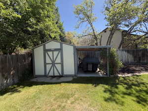 Backyard featuring a shed with an attached covered storage area, surrounded by a wood fence, mature trees, and a grassy lawn