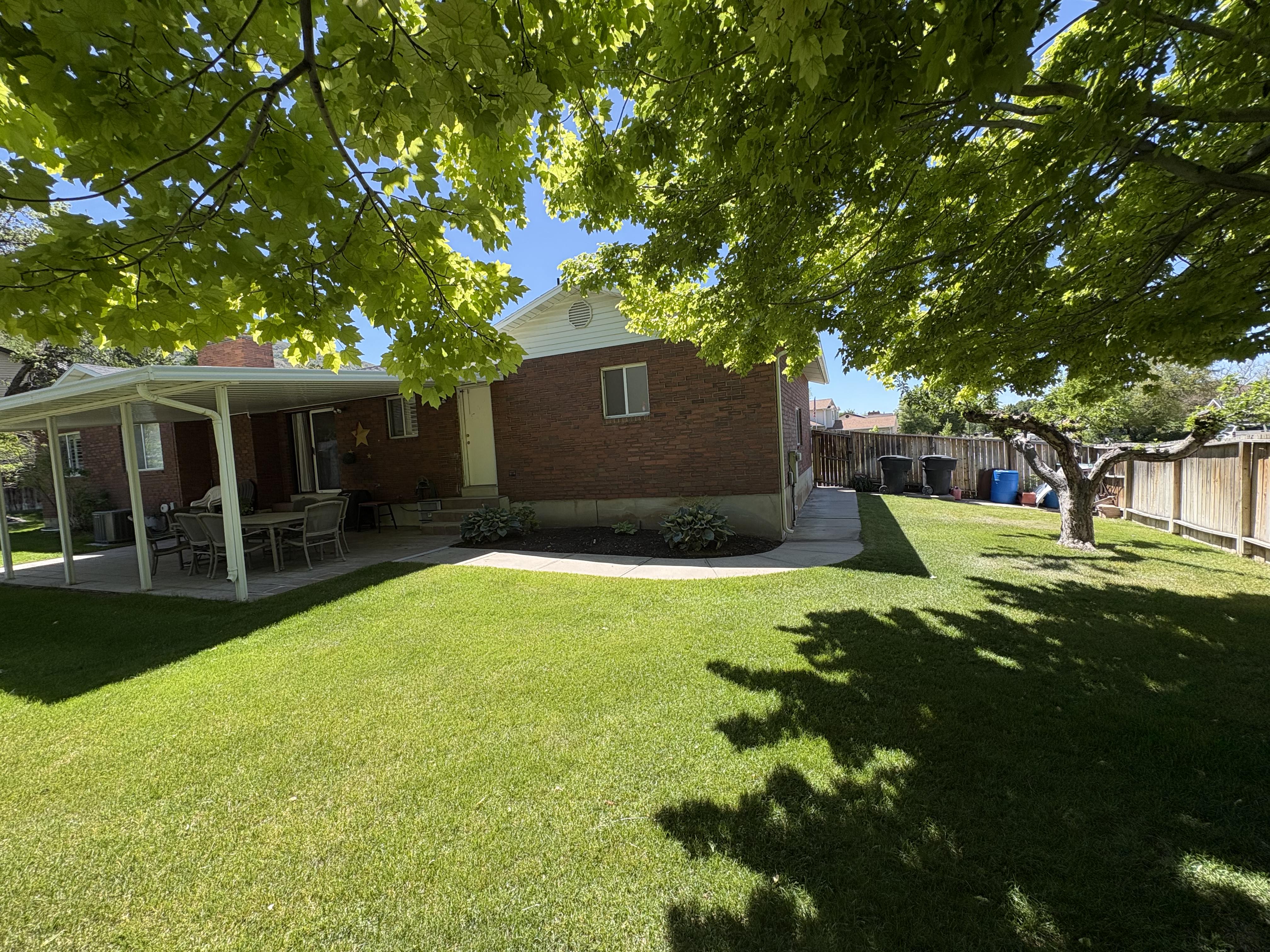 Expansive backyard featuring a lush lawn, mature shade tree, and a covered patio with a paved surface