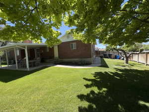 Expansive backyard featuring a lush lawn, mature shade tree, and a covered patio with a paved surface